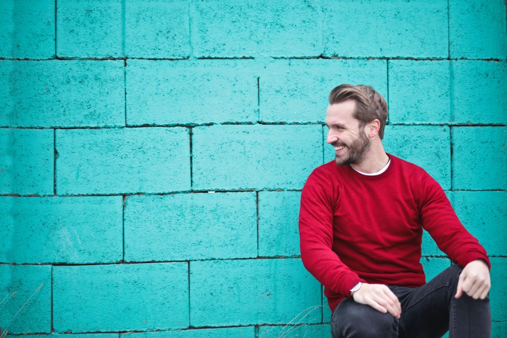 A man leaning on a wall and sitting on a bench smiling