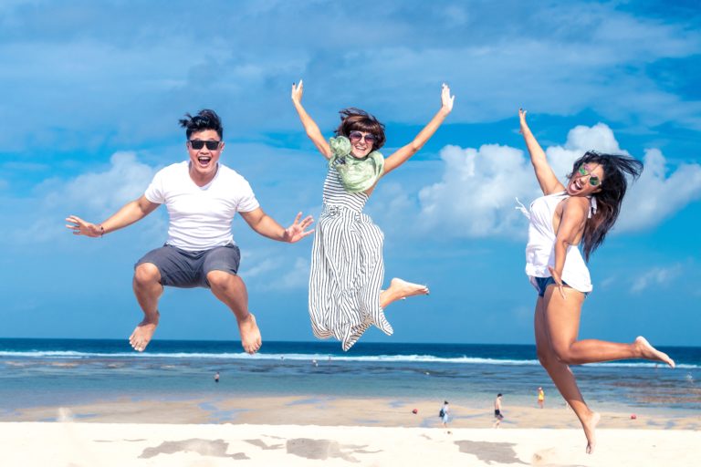Three people jumping and looking happy on a beach